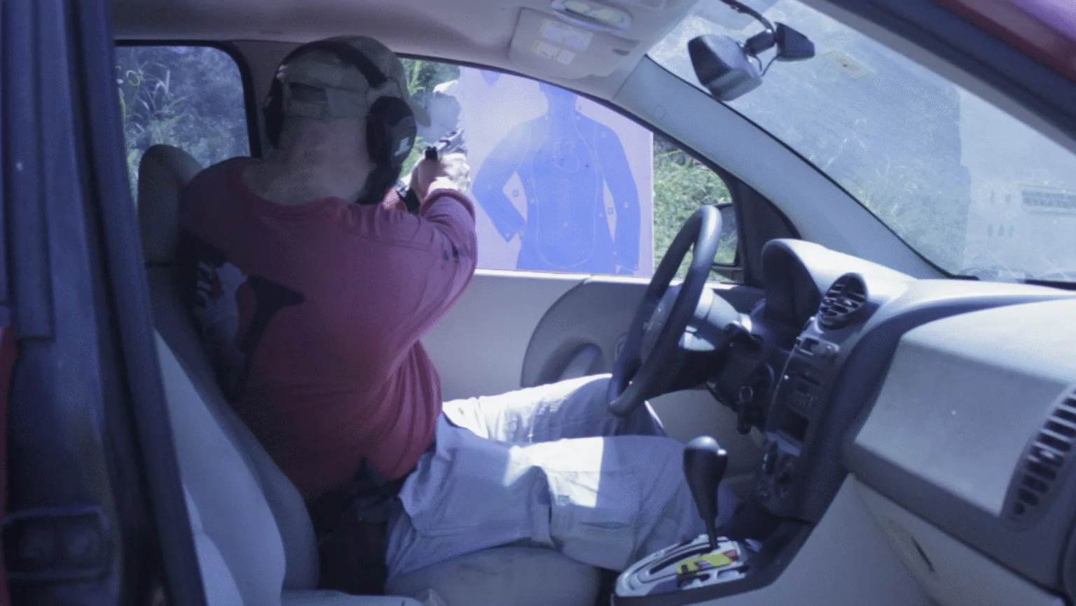 Man fires a handgun from a car toward a paper target.