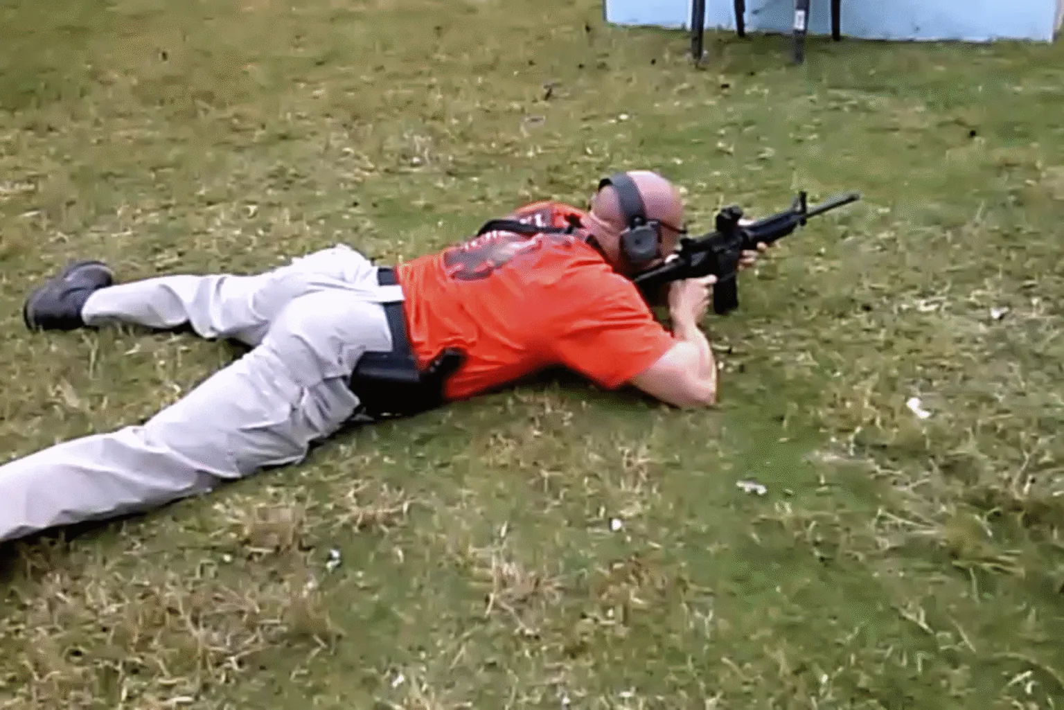 Man aims a rifle while lying prone on an outdoor range.