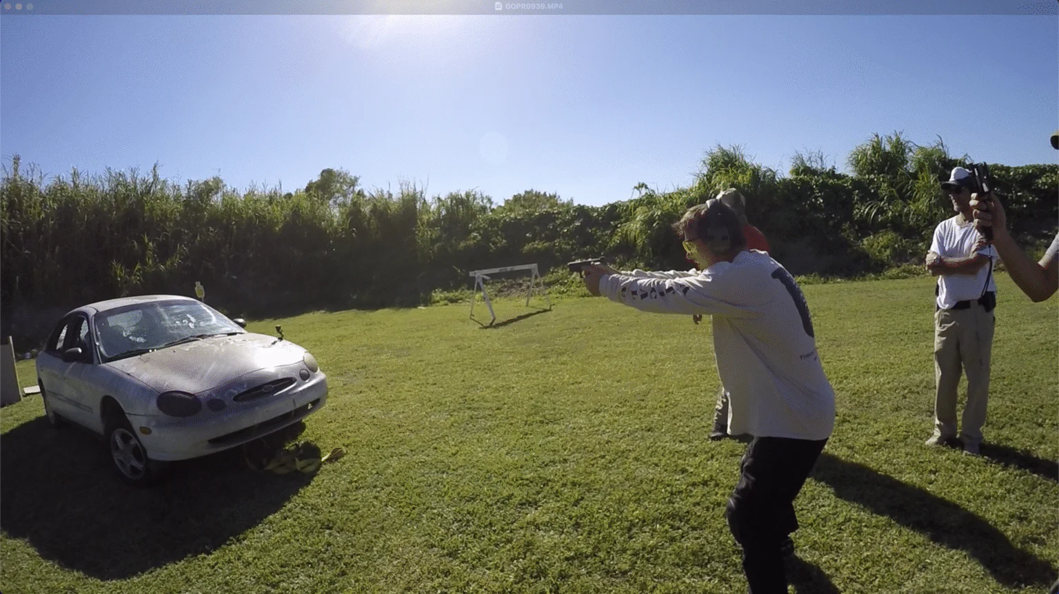 Woman fires a handgun beside a vehicle during outdoor training.