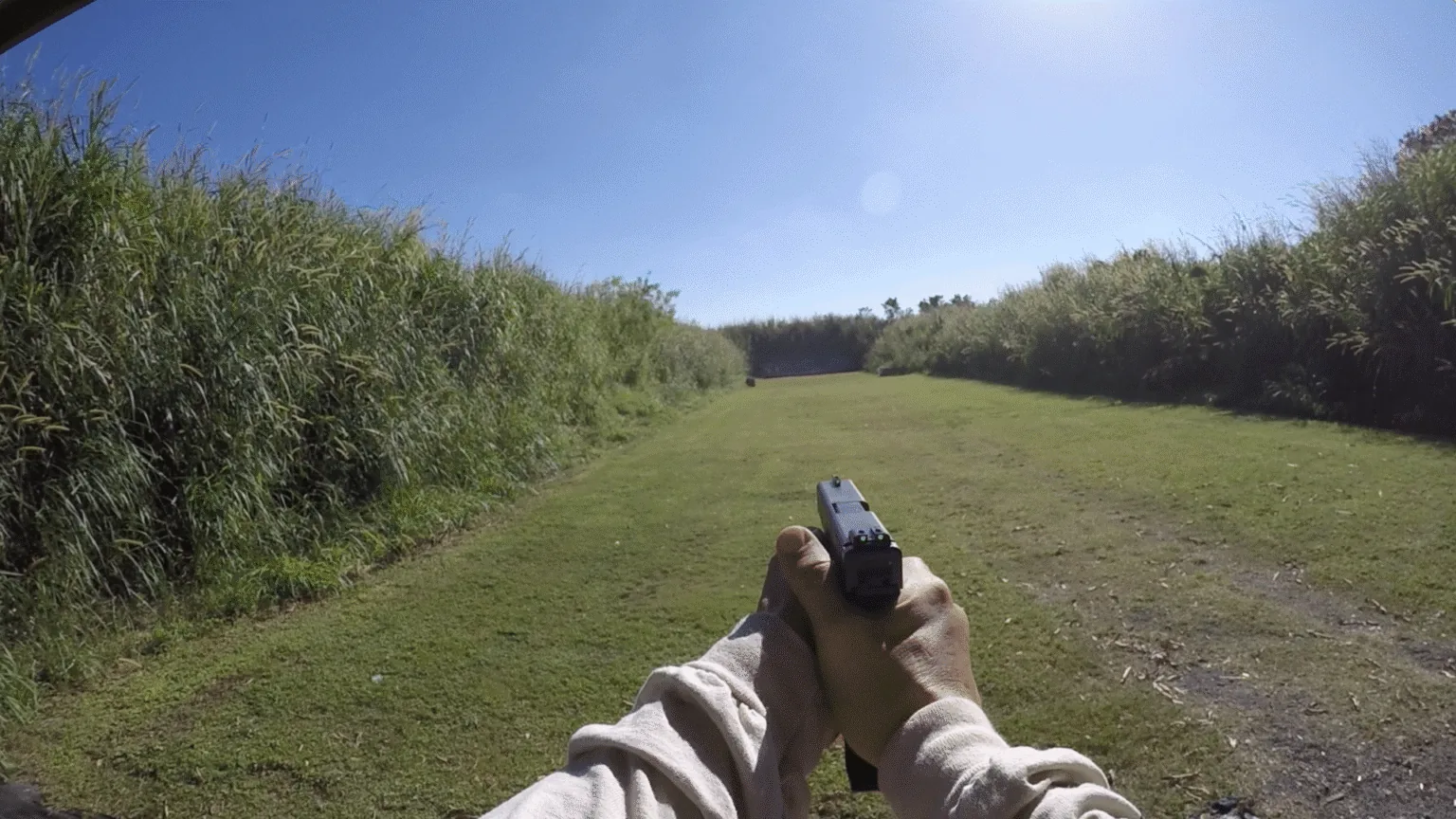 First-person view of a handgun aimed down an outdoor range.