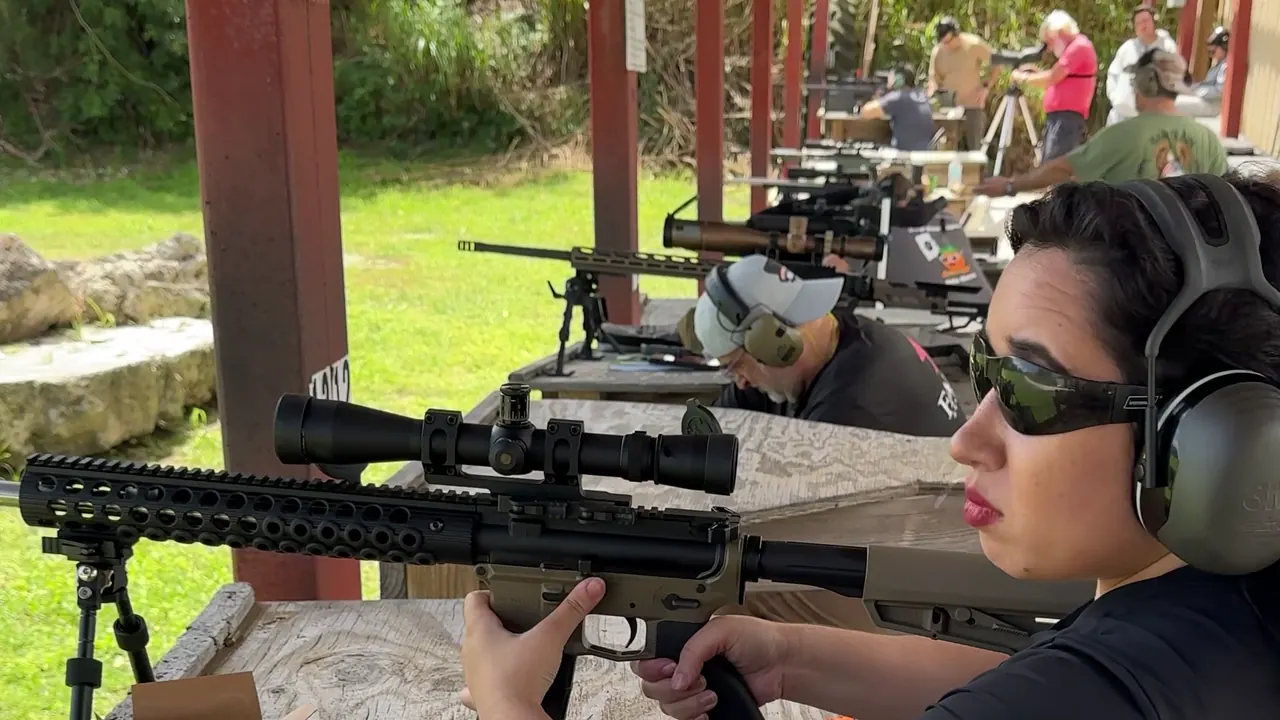Woman in ear and eye protection firing a scoped precision rifle from a shooting bench