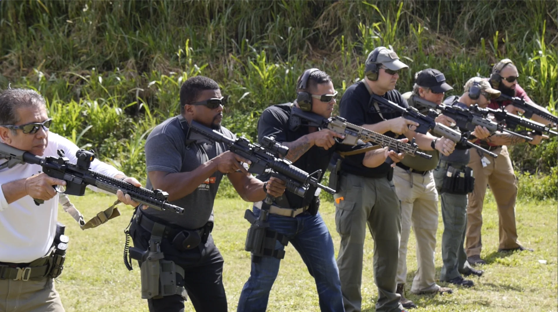 Six students aim rifles in a line on an outdoor range.