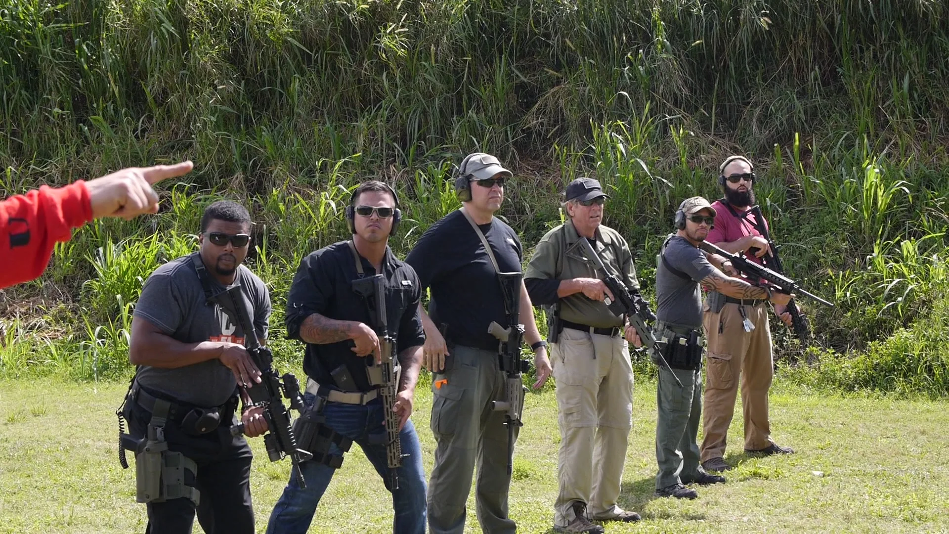 A line of armed students listening as a Tactical U instructor points downrange during a class