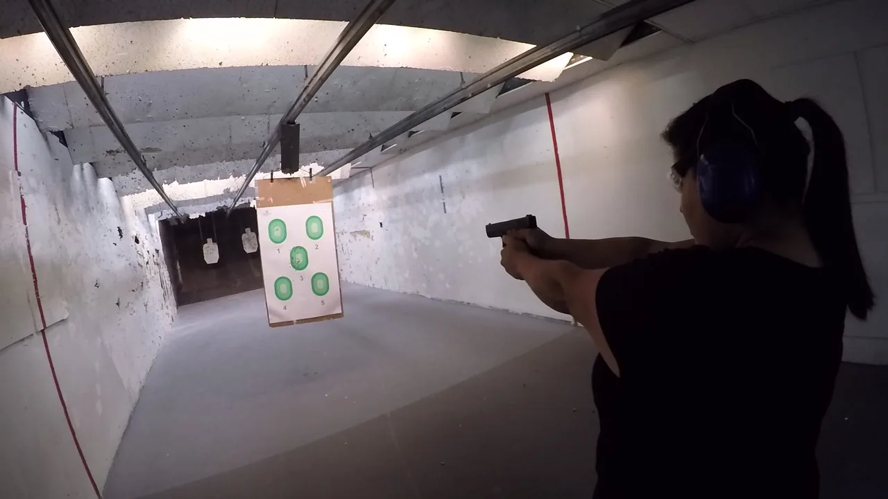 Student with ear protection aiming a pistol at a paper target on an indoor range