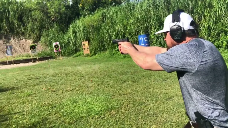 Student in a white cap firing a pistol on an outdoor range