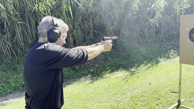 Student firing a pistol on an outdoor range with brass in the air