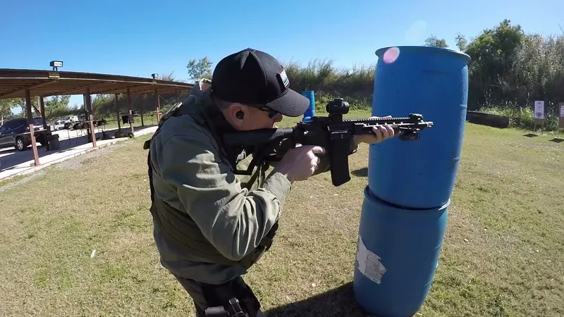 Student firing an AR-style rifle around a blue barrel barricade