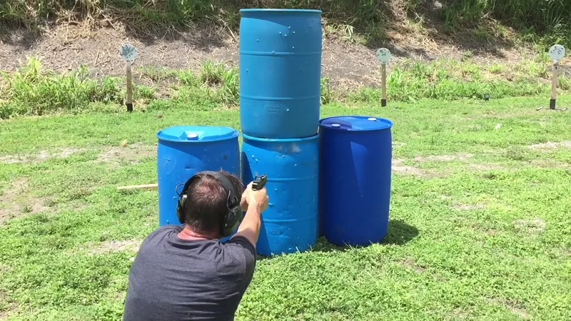 Student kneeling behind stacked blue barrels with a pistol