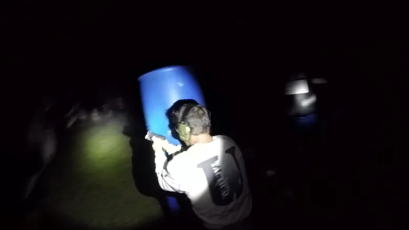 Student in a Tactical U shirt shooting past a blue barrel at night