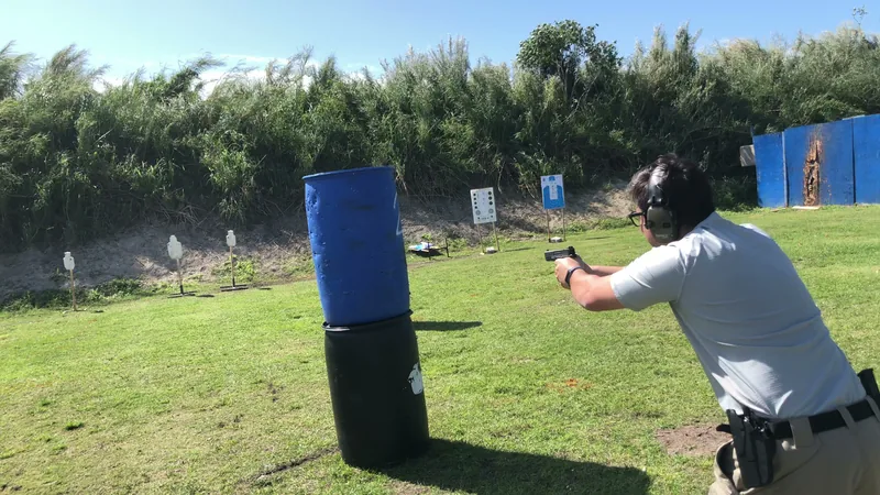 Student shooting a pistol from behind blue barrel cover