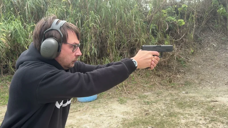 Student in a dark hoodie aiming a pistol at the range