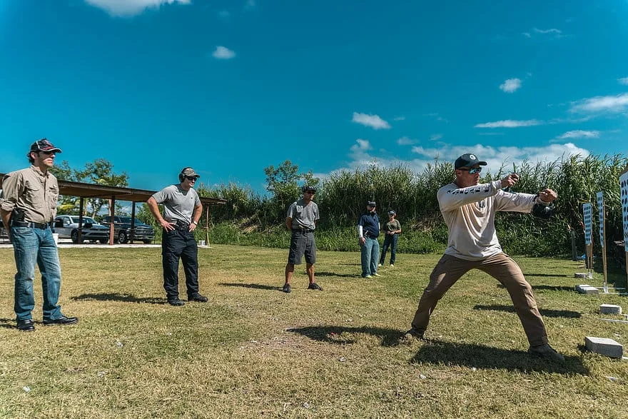 Tactical U instructor demonstrating a pistol shooting stance on the outdoor range line while students watch