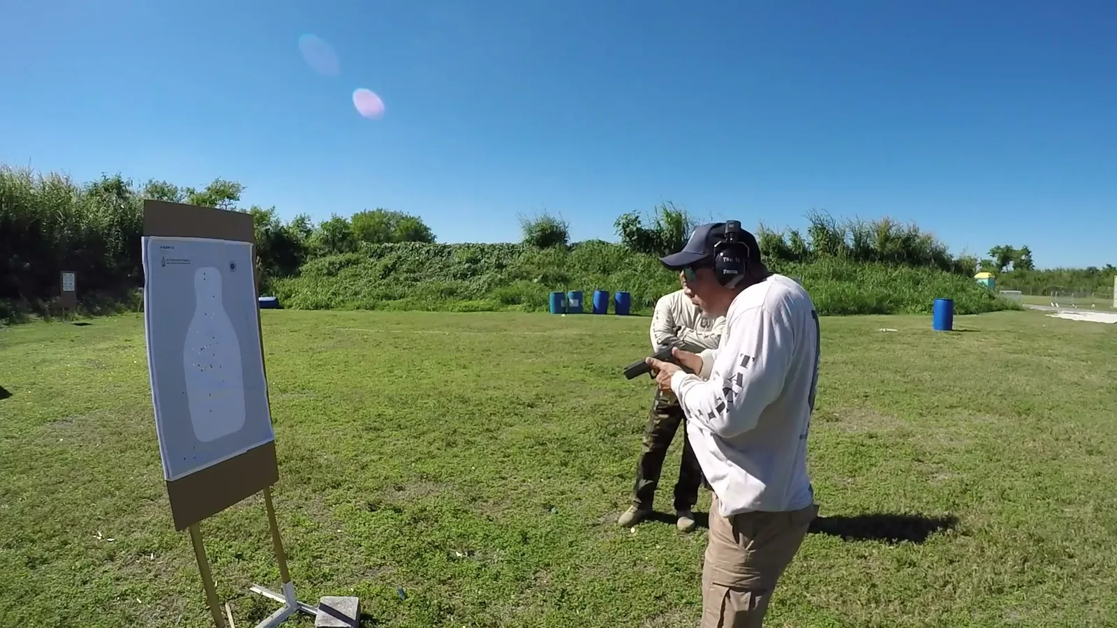 Shooter firing a pistol at a paper target from close range on an outdoor range