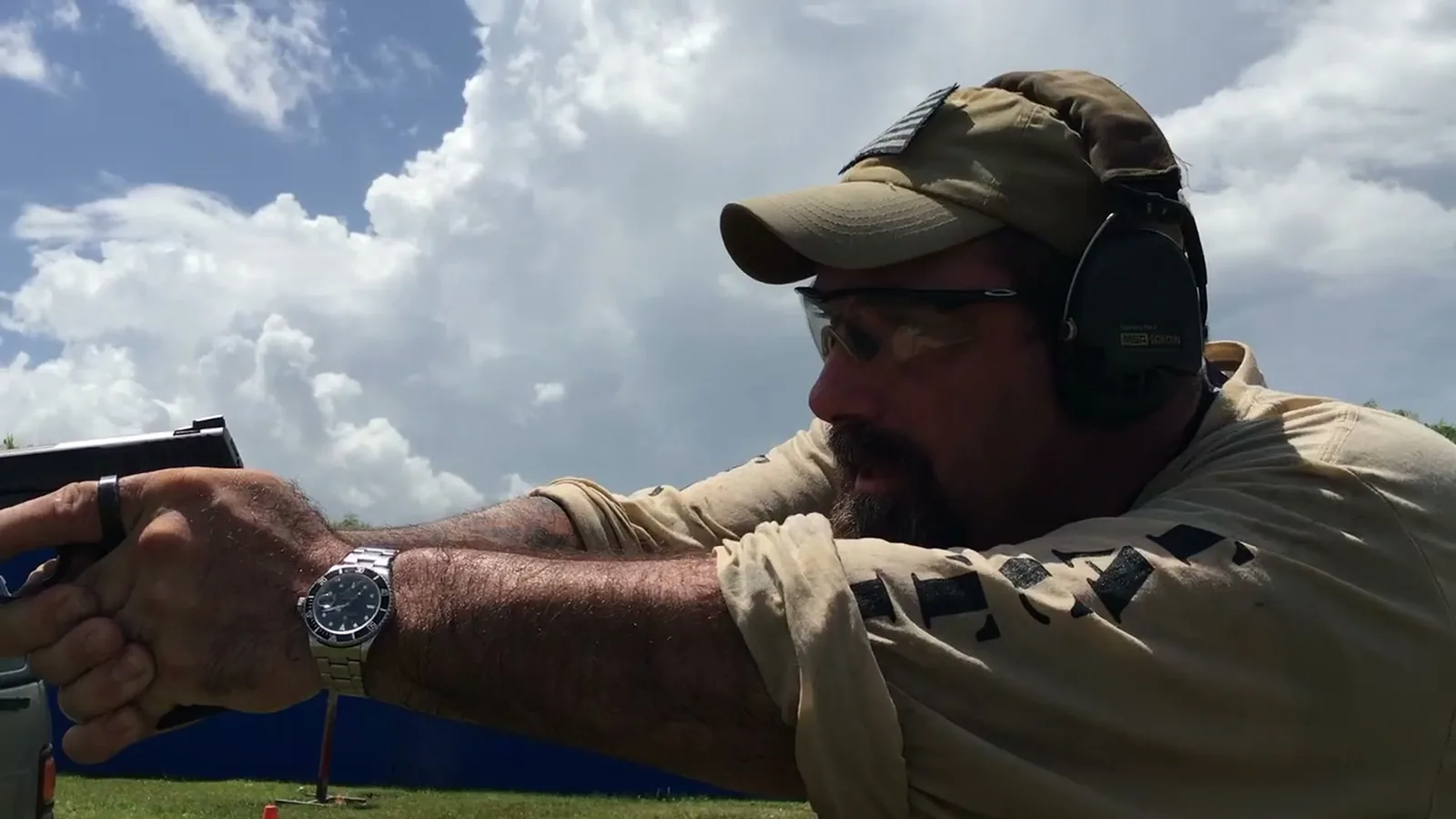 Close-up of a shooter in a cap and ear protection aiming a pistol with both hands
