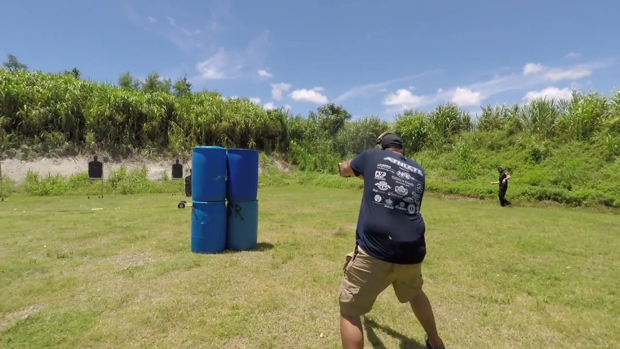 Shooter firing a pistol from behind barrel cover on an outdoor range