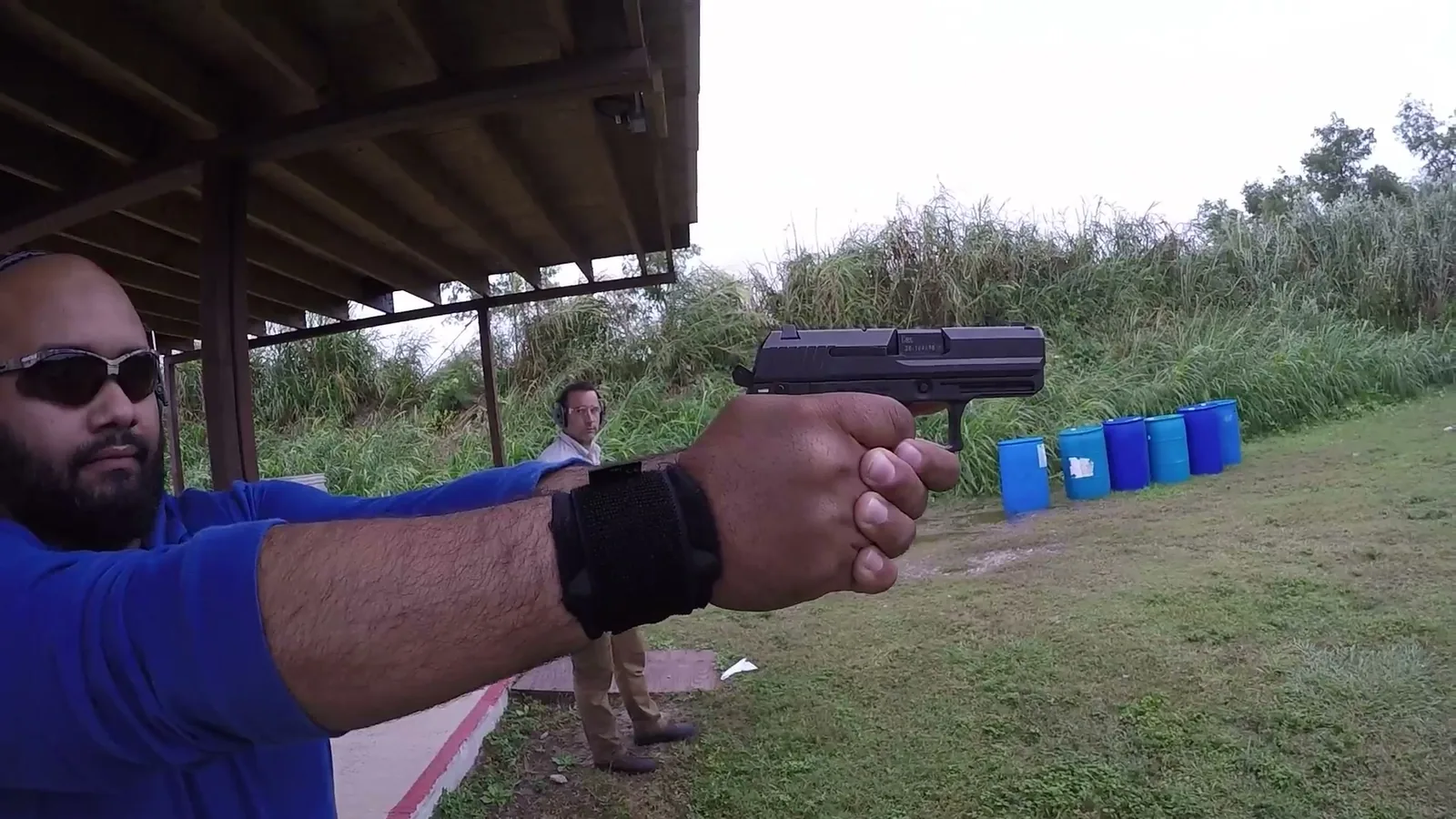 Close-up of a shooter's two-hand pistol grip and sights under a covered firing line