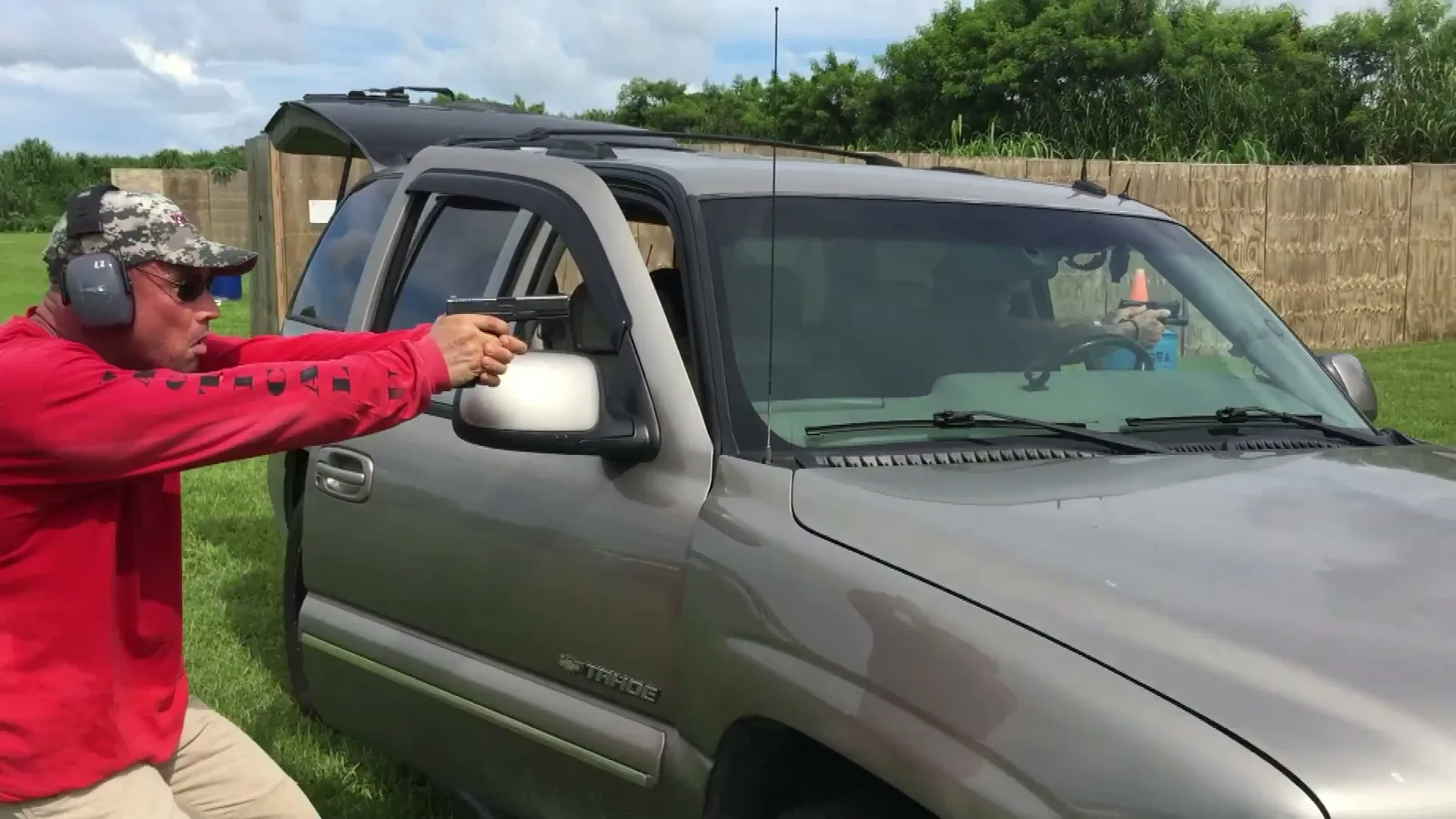 Tactical U instructor in a red shirt aiming a pistol over an open vehicle door during a vehicle tactics drill