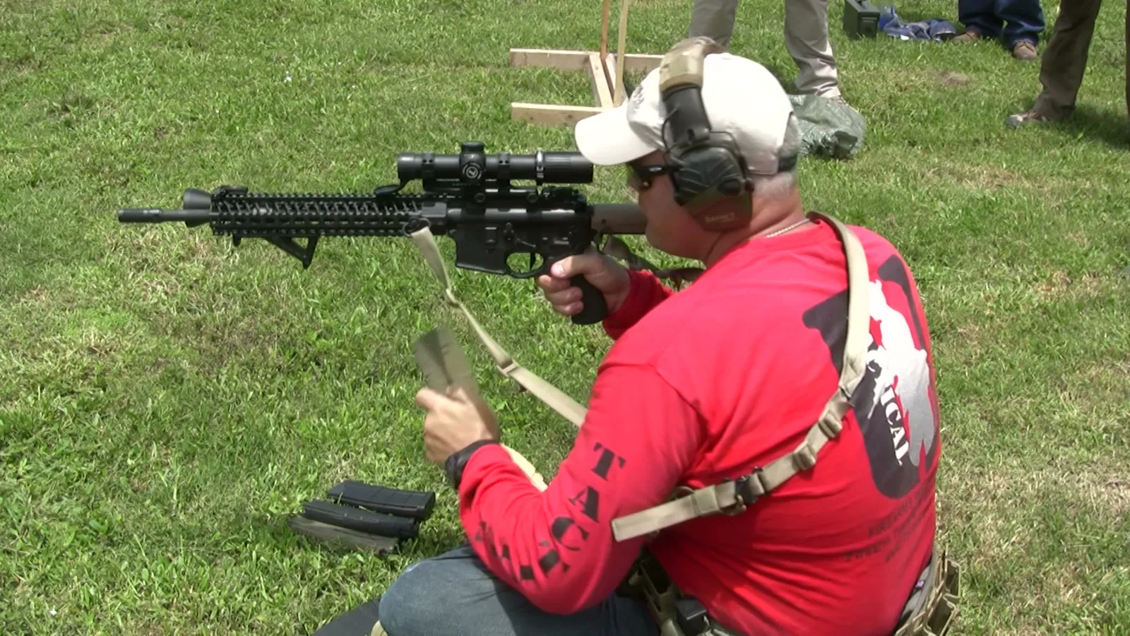 Tactical U instructor in a red Tactical U shirt firing a scoped rifle on an outdoor range