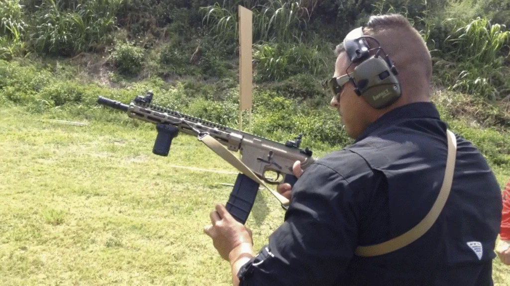 A student handling a rifle while wearing hearing protection on an outdoor range
