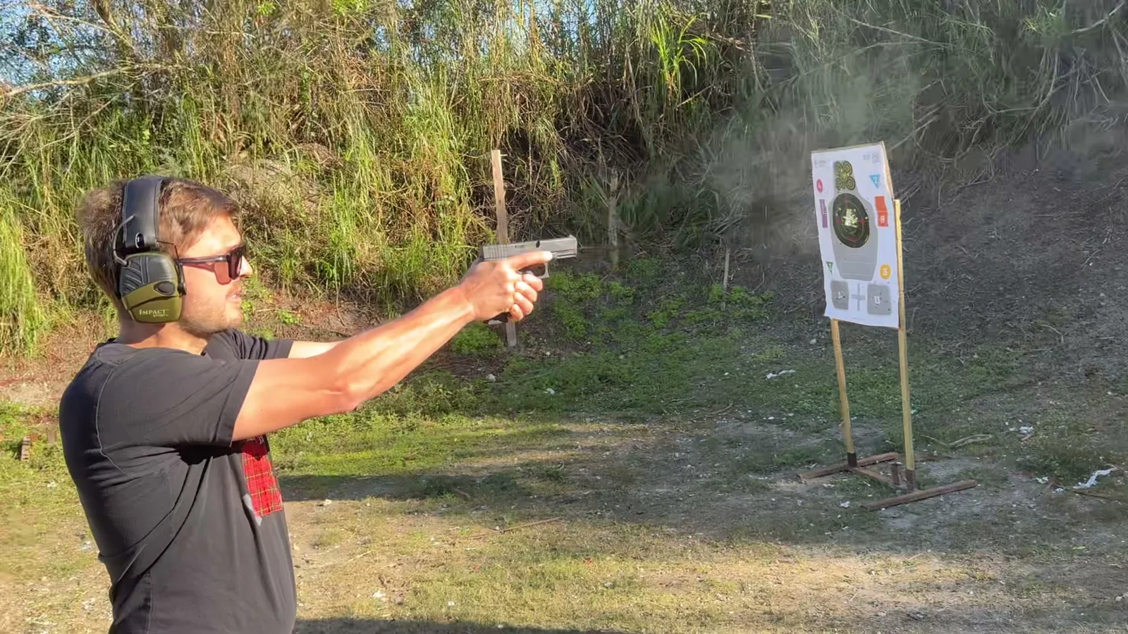 Tactical U student firing a pistol at a target on an outdoor South Florida range, wearing eye and ear protection