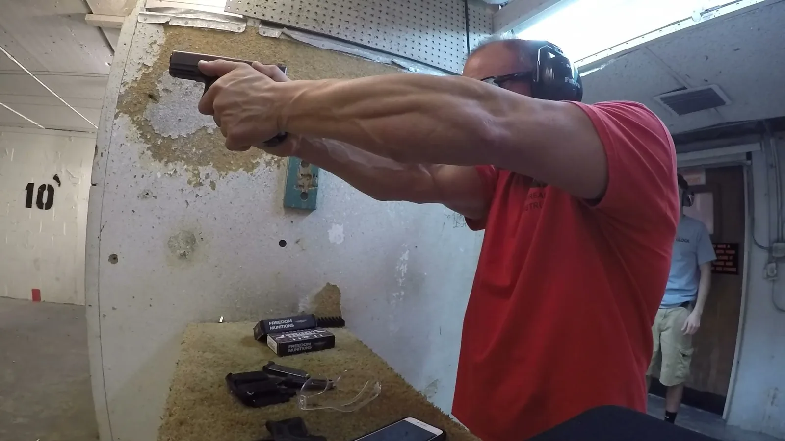 Shooter with ear protection firing a pistol at a close target on an indoor range