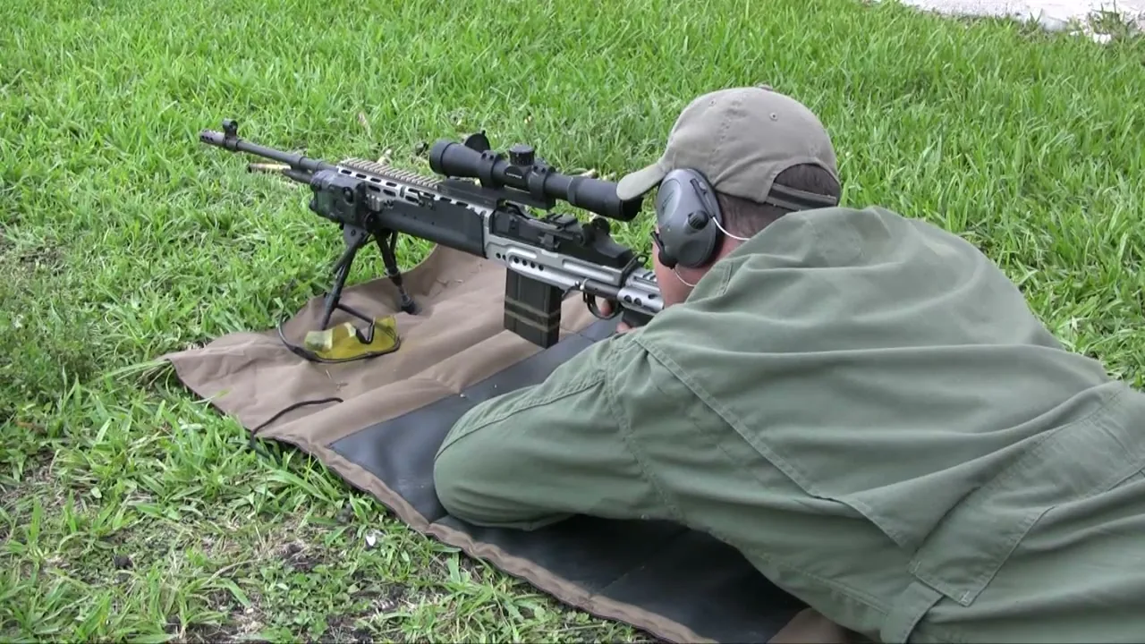 Shooter in the prone position aiming a scoped precision rifle on a ground mat