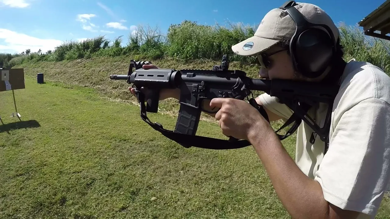 Rifle student with eye and ear protection aiming an AR-style rifle on an outdoor range