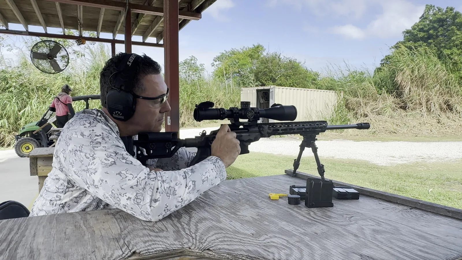 Student at a shooting bench with a scoped rifle on a bipod, holding a consistent cheek weld