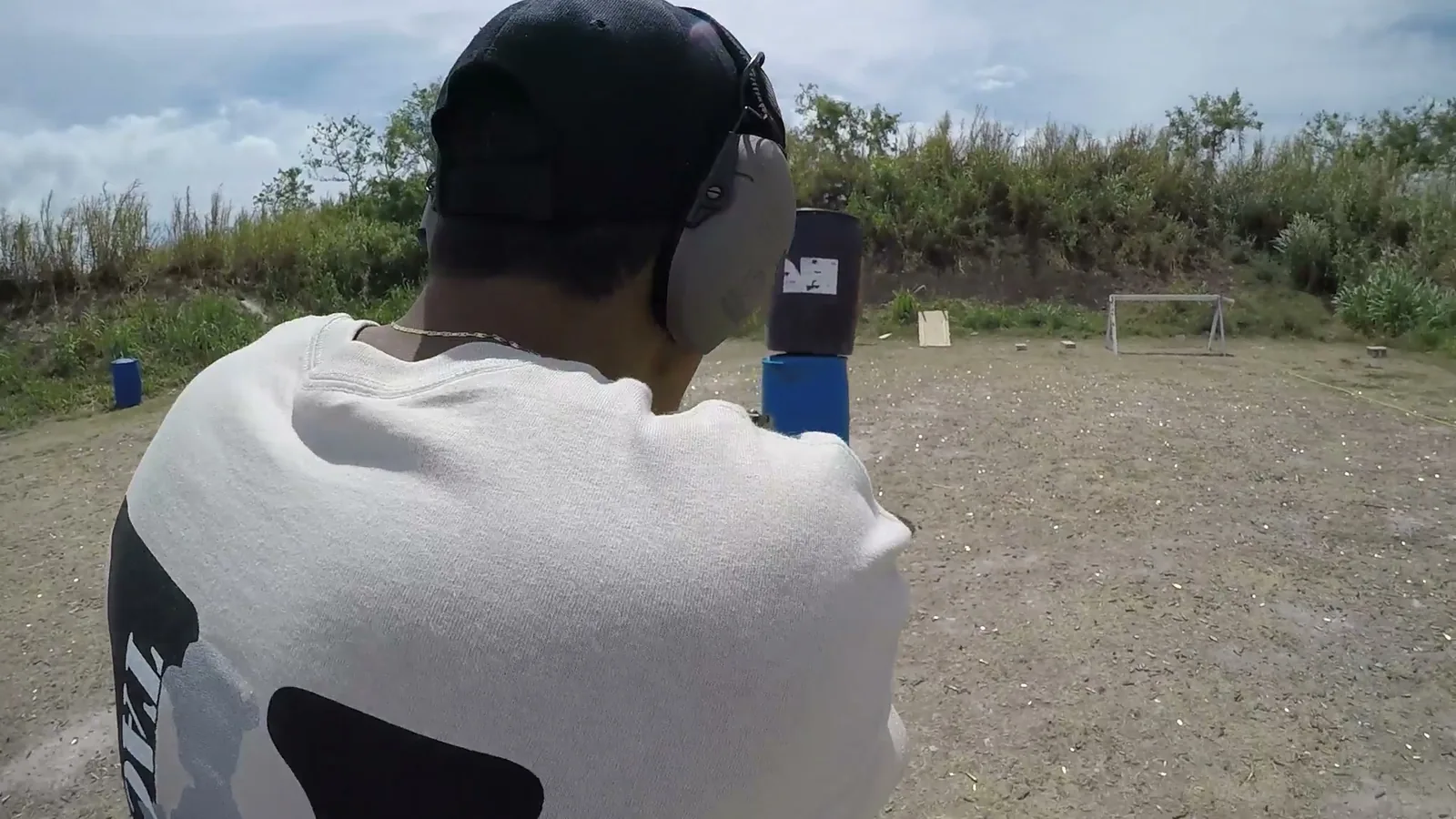 Shooter in a Tactical U shirt and ear protection aiming a handgun at targets on an outdoor range