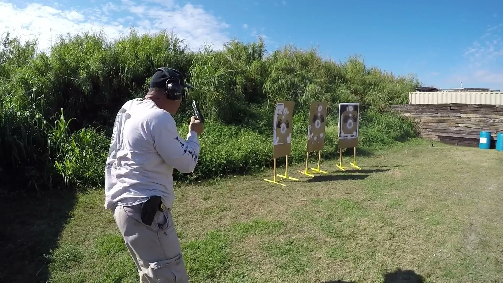 Instructor firing a pistol while moving toward paper targets on an outdoor range