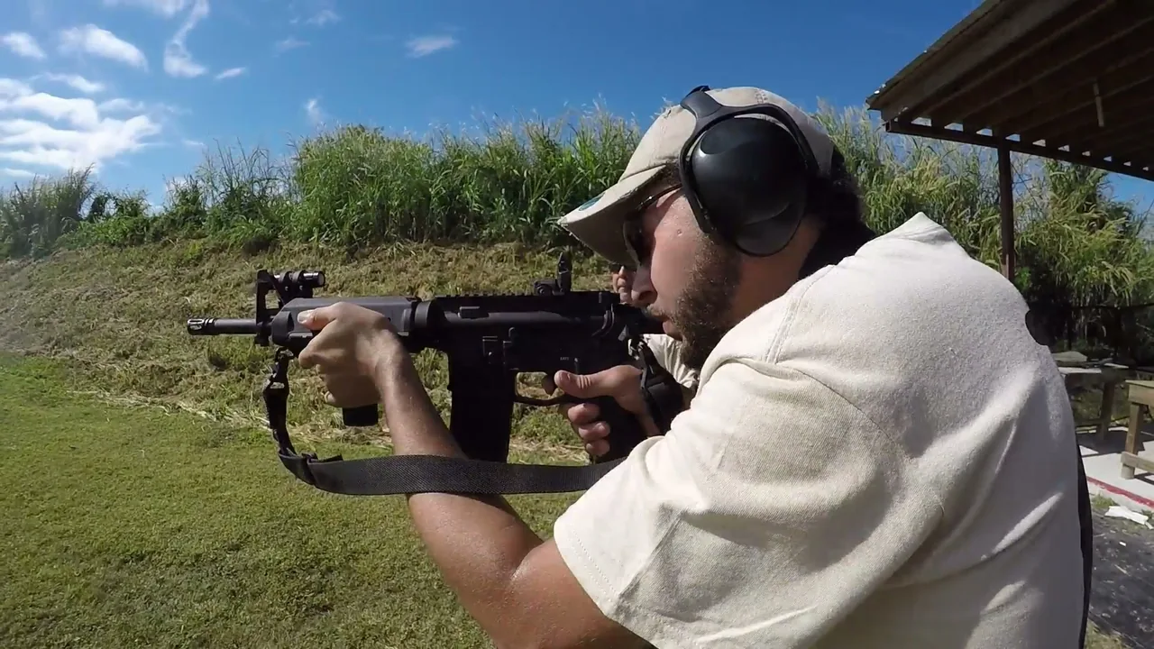 Rifle student with ear protection aiming an AR-style rifle from the covered firing line during tactical rifle fundamentals