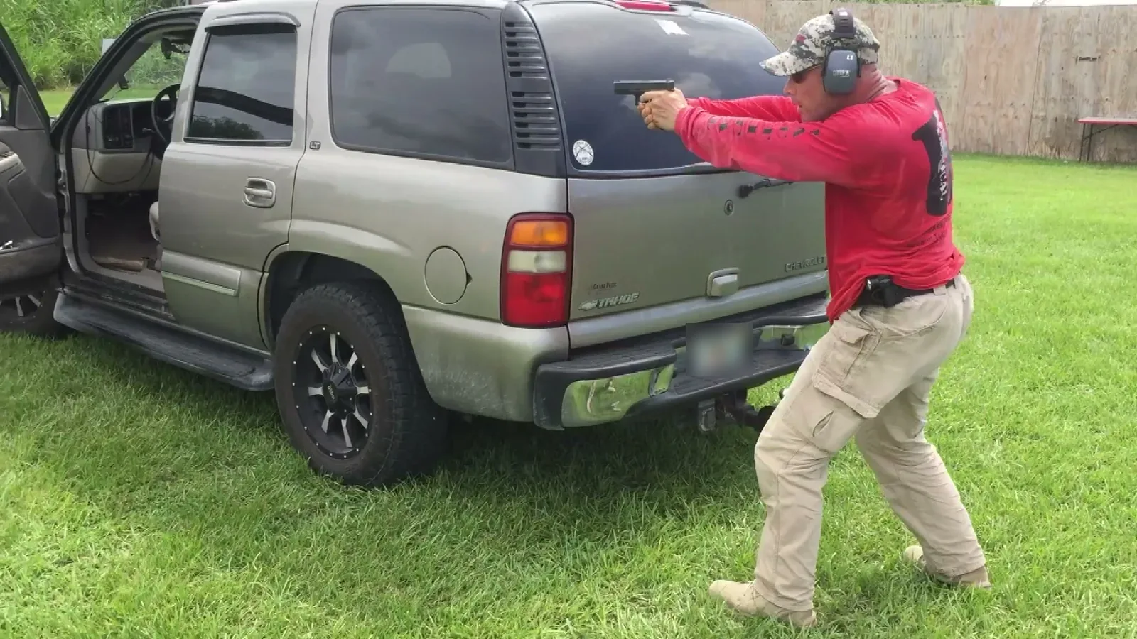 Tactical U instructor in a red Tactical U shirt aiming a pistol from behind an SUV during vehicle tactics training