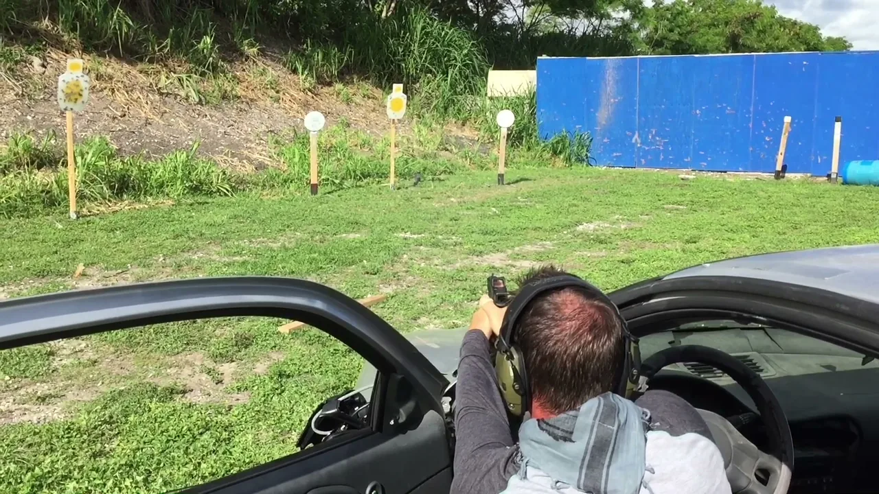 Student with eye and ear protection firing a handgun from an open car door during Tactical U vehicle tactics training